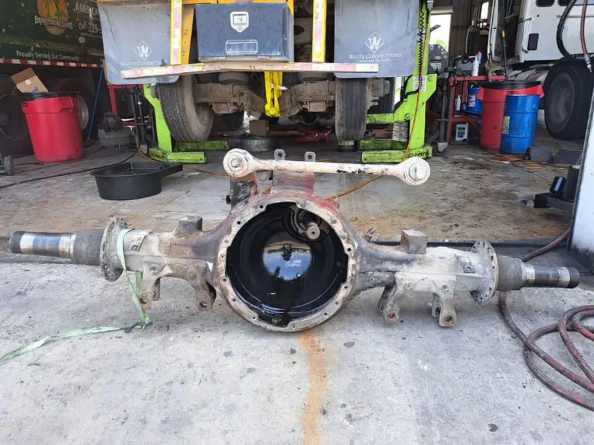 A disassembled heavy-duty truck differential housing sits on a garage floor during a major repair.