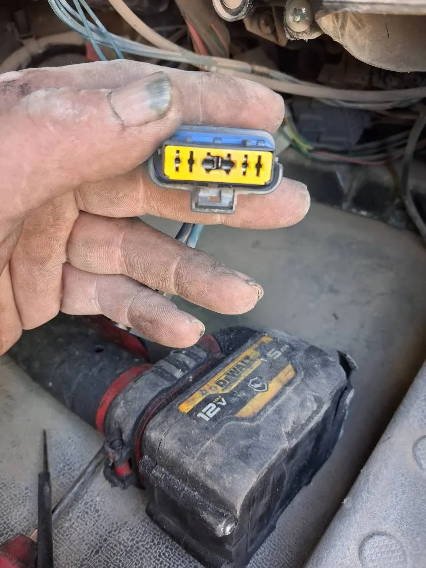 A heavy-duty mechanic holds a yellow and blue electrical connector during a roadside diagnostic repair.