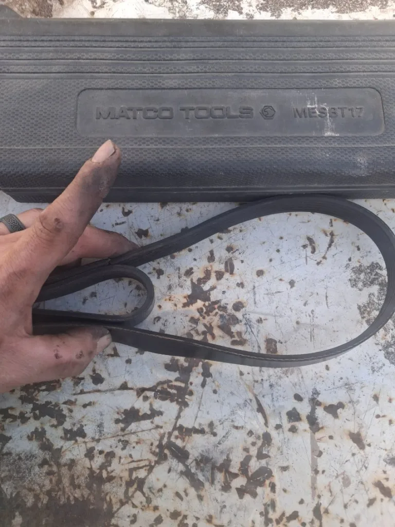 Grease-stained hand holding a black engine drive belt near a Matco Tools case during a mobile truck repair.
