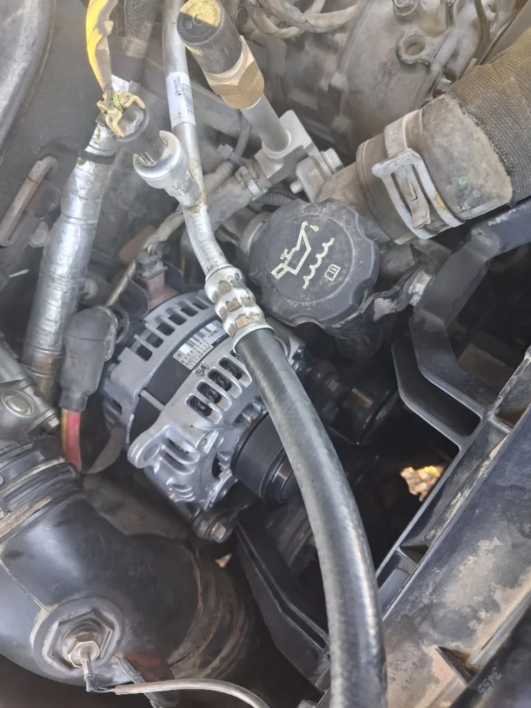 Newly installed alternator in a commercial truck engine bay during a roadside repair service in Mohave Valley.