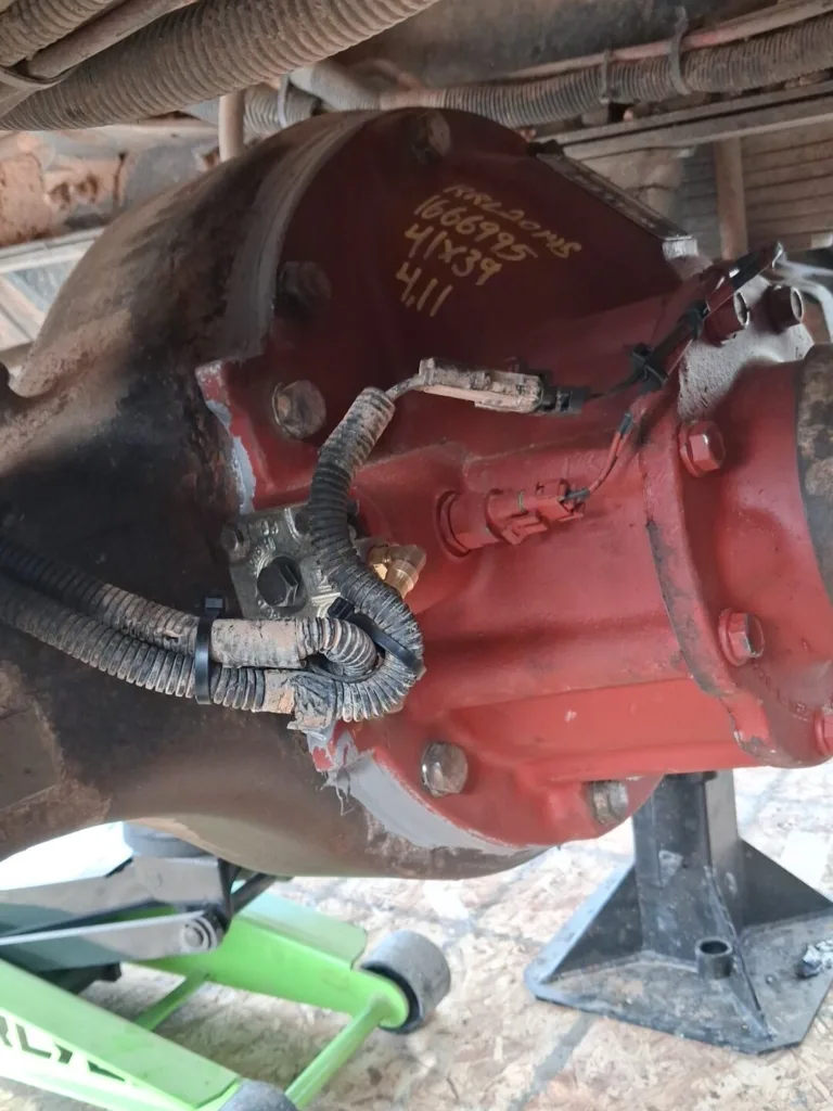 Close-up of a red commercial truck differential housing with wiring harnesses and gear ratio markings.