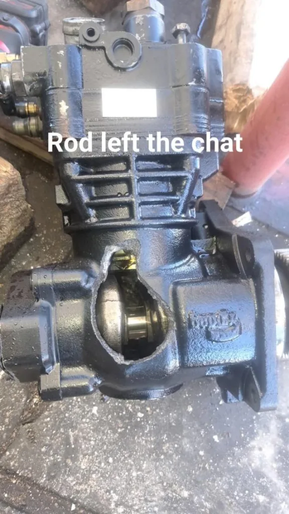 Damaged Bendix truck air compressor with a large hole in the metal housing revealing internal parts.
