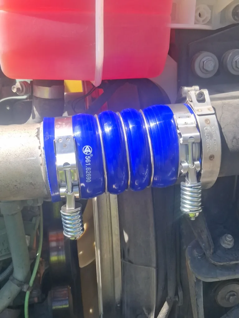 Blue silicone turbo hose secured with heavy-duty spring T-bolt clamps on a commercial truck diesel engine.