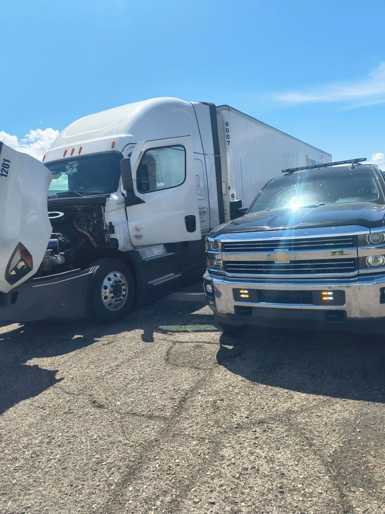White semi-truck with open hood receiving mobile diesel repair service from a TRT Roadside pickup truck.