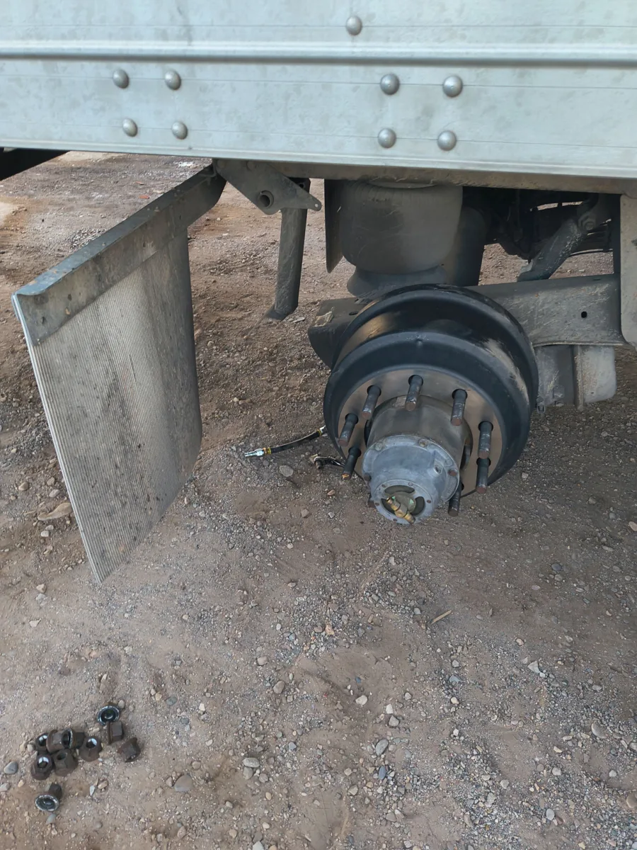 Semi-truck trailer wheel hub and brake drum exposed during a mobile roadside repair on a gravel shoulder.