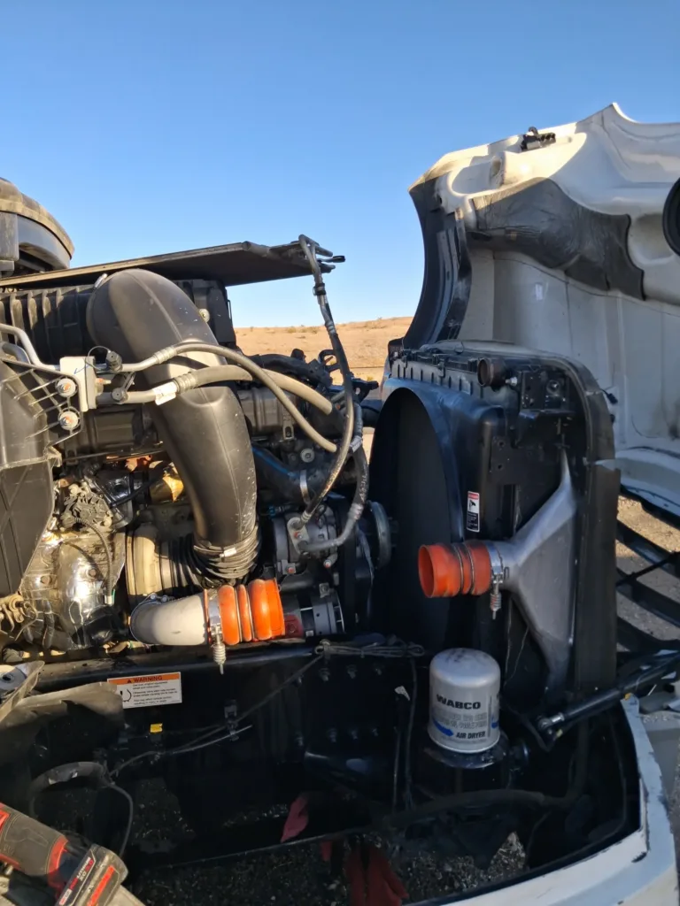 Open hood of a semi-truck showing a diesel engine, WABCO air dryer, and radiator during roadside repair.